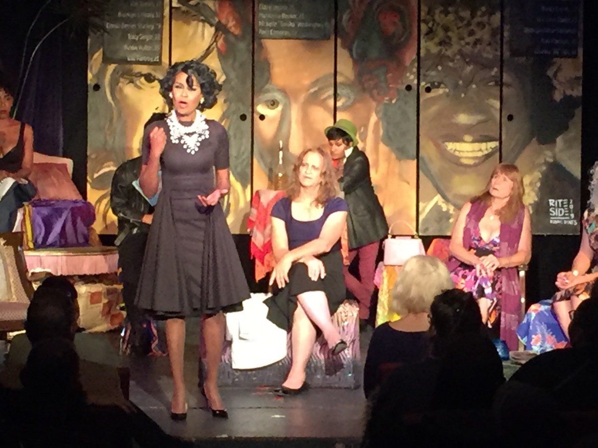Young woman in a dark dress speaking on stage with seated audience members.