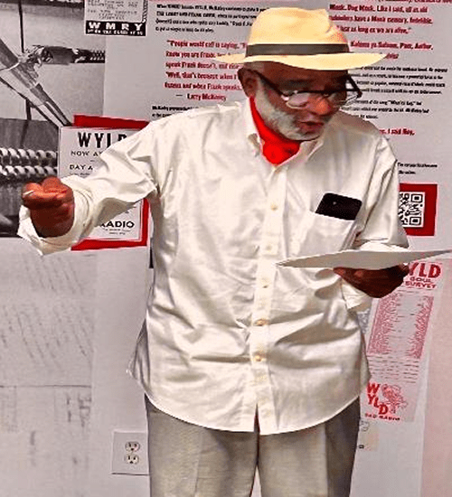 Elderly man wearing a hat and mask holding a plate and a cup.