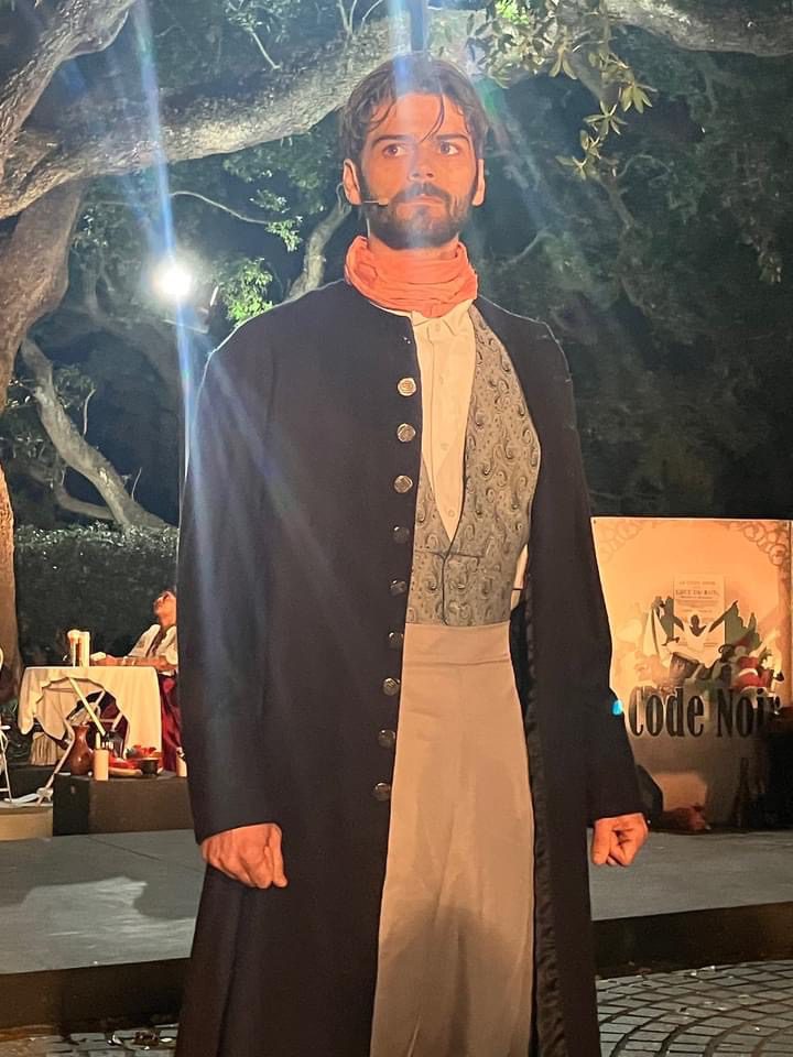Man in traditional attire standing outdoors at night with warm lighting.