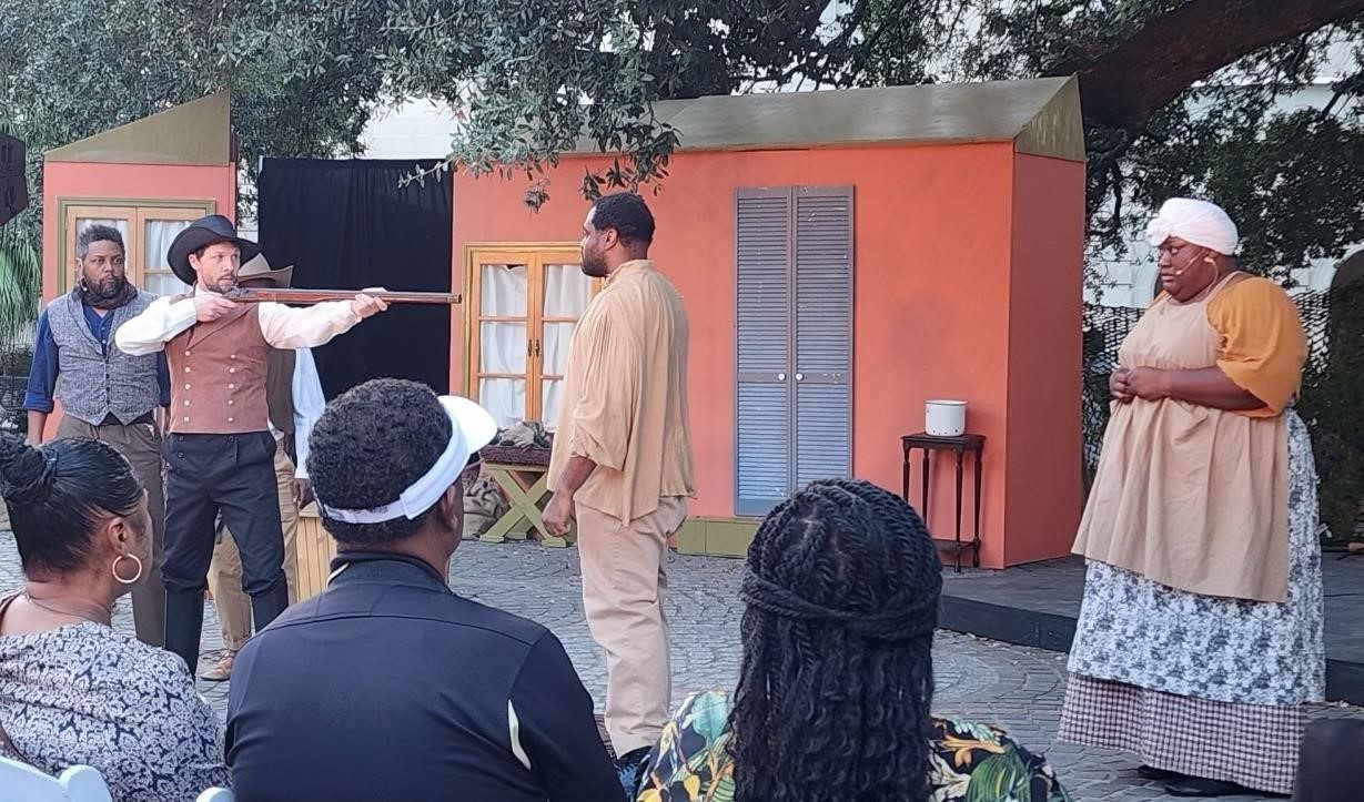 Actors perform on a colorful outdoor stage with an audience watching.
